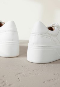 Baskets basses blanches en cuir, avec une texture lisse, des talons arrondis et une semelle plateforme blanche épaisse avec des accents cousus.