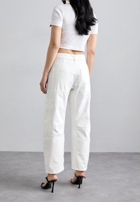Pantalones cargo blancos de corte relajado y múltiples bolsillos, combinados con una camiseta corta de canalé blanca ajustada y sandalias de tacón alto negras.