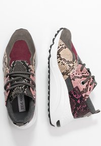 Sneaker chunky con materiali misti, inclusi camoscio e stampa pitone in grigio, burgundy, rosa e bianco, caratterizzati da suole bianche spesse e lacci scuri.