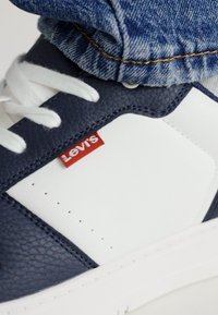 Skórzane tenisówki z granatową cholewką i białymi akcentami, teksturowanymi panelami oraz czerwonym logo Levi's. Białe sznurowadła i minimalne perforacje.