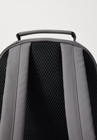 Mochila gris con un respaldo acolchado de malla negra, correas de hombro ajustables y un asa superior resistente para un fácil transporte.