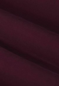 Diep bordeauxkleurige stof gevouwen, die een soepele textuur en fijn diagonaal weefpatroon in close-up detail laat zien.