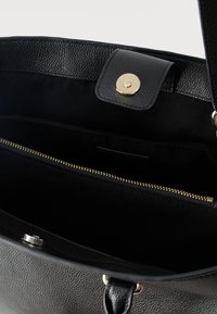 Εσωτερικό μαύρης δερμάτινης τσάντας με φερμουάρ σε θήκη και μαγνητικό κούμπωμα σε υφασμένο άκρο.