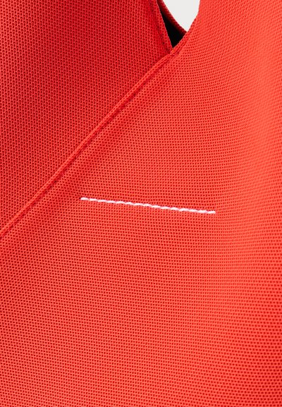 Κοντινό πλάνο κόκκινου υφάσματος με υφή, με λοξή ραφή και μια μικρή, οριζόντια γραμμή λευκής ραφής.