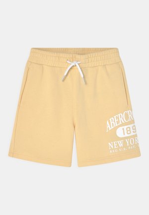 Lysegule afslappede shorts med elastisk linning, hvid snor, sidelommer og hvid tekst på venstre ben.