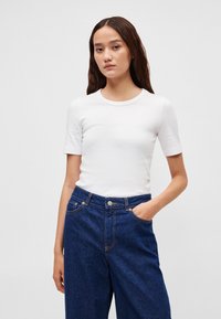 Λευκό κοντομάνικο μπλουζάκι με στρογγυλή λαιμόκοψη, σε συνδυασμό με μπλε τζιν παντελόνι ψηλόμεσο με εμφανείς ραφές και τσέπες.