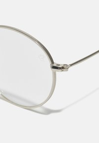Ochelari metalici rotunzi cu lentile clare. Cadru subțire din metal argintiu, prezentând accente texturate și un zăvor lustruit pentru o ajustare flexibilă.