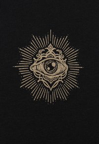 Black textile featuring a central gold eye design surrounded by ornate patterns and radiating lines, with a textured knit surface.