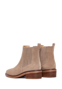 Bottines en daim beige avec des panneaux latéraux en élasthanne, bout rond et un talon en bois empilé. Texture lisse avec des accents à nervures verticales.