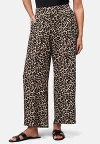 Pantalon large à imprimé léopard en tissu léger, avec une taille élastique et des poches latérales, dans une palette de couleurs neutres beige et marron.