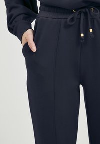 Marina joggerbyxor i mjukt tyg, med resårmidja och dragsko, sidfickor och detaljer i guld.