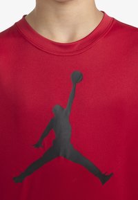 Camisa roja de manga corta con cuello redondo y una prominente silueta negra de un atleta saltando impresa en la parte frontal.