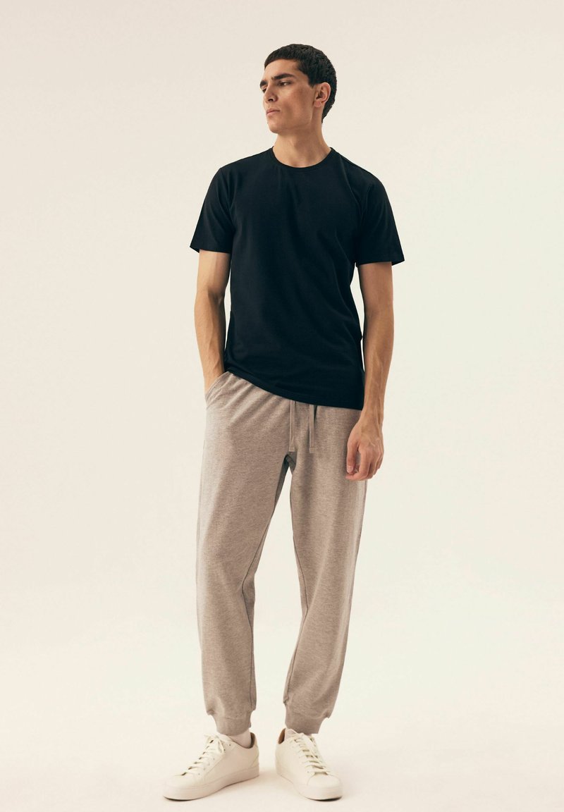 Schwarzes kurzärmliges T-Shirt, graue Jogginghose und weiße Turnschuhe. Das T-Shirt hat einen runden Halsausschnitt; die Hose hat einen elastischen Bund und Bündchen.