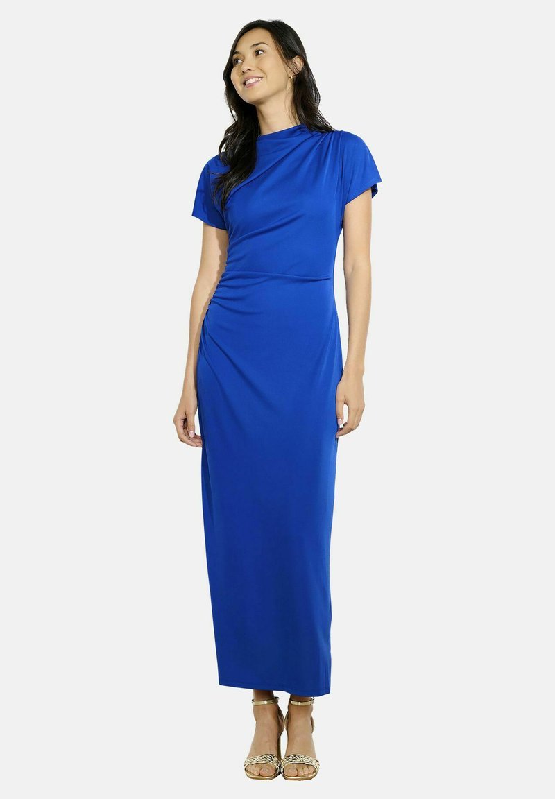 Modrá maxi šaty s krátkymi rukávmi, drapovaný dizajn, hladká textúra a naťahovanie v oblasti pásu. Nosené s remienkovými zlatými sandálmi.