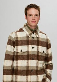 Brun og creme ternet flanneljakke med krave, der har to forreste lommer og knaplukninger.