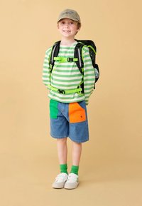 Striped long-sleeve shirt in green and white, denim shorts with green and orange patches, green socks, white sneakers, and a gray cap.