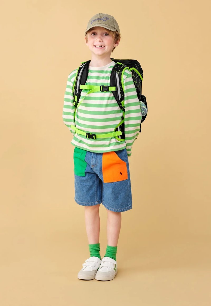 Striped long-sleeve shirt in green and white, denim shorts with green and orange patches, green socks, white sneakers, and a gray cap.