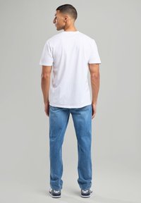 Camiseta blanca de algodón con escote redondo, combinada con unos jeans de mezclilla azul claro. Corte casual con aberturas de pierna estándar.