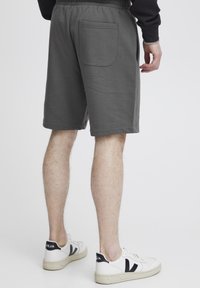Grå bomulds shorts med elastisk talje og en baglomme. Shortsene er knælange og har en glat overflade. Båret med hvide sneakers.