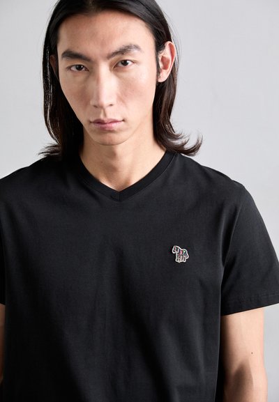 T-shirt en coton noir avec un design en col en V, mettant en avant un logo animal brodé coloré sur la poitrine gauche. Texture douce, manches courtes.