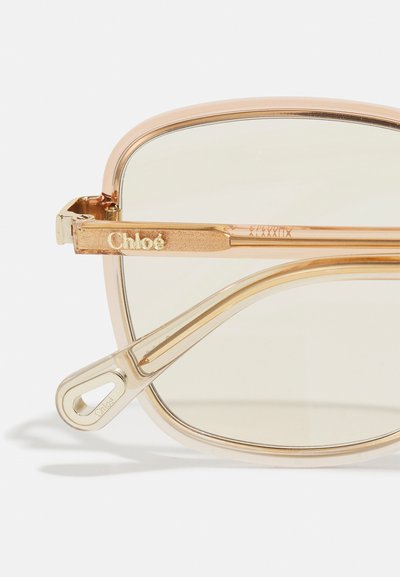 Chloé solglasögon med en lätt bärnstensfärgad acetatrams, rektangulär form, metallaccenter i guldton och ljusa linser. Logotypen är graverad på skalmen.