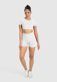 Weißes, kurz geschnittenes Sportoberteil und hochgeschnittene Shorts, aus glattem Stoff mit dehnbarem Schnitt, minimalen Nähten und Logodetail.