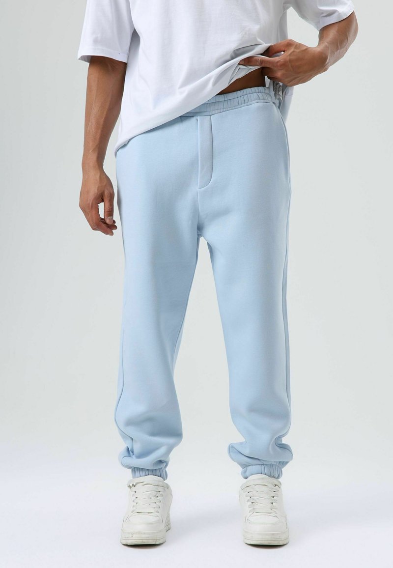 Lichtblauwe sweatpants van zachte stof, voorzien van een elastische tailleband en gebandevoete enkels. Gecombineerd met witte sneakers.