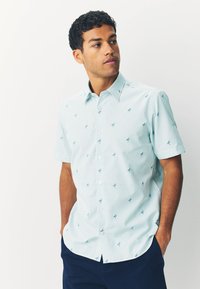 Camicia azzurro chiaro a maniche corte con bottoni, a righe verticali e piccoli motivi a foglia. Realizzata in un tessuto liscio e leggero.