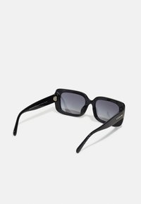 Juodos stačiakampės saulės akinius su gradientiniais lęšiais, stambiais plastikiniais rėmeliais ir sidabriniu akcentu ant šventykloje, kuriame užrašyta prekės ženklo pavadinimas.