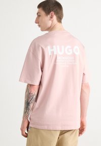 Light pink cotton t-shirt featuring large white "HUGO" lettering on the back, short sleeves, and a relaxed fit.