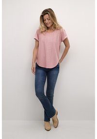 Haut rose clair à manches courtes avec motif en œillet, encolure ronde et ourlet incurvé, associé à un jean évasé bleu et des bottines beige.