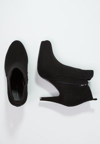 Černé kotníkové boty na vysokém podpatku z nubuku se zapínáním na zip na boku. Mají špičatou špičku a kovový akcent na podpatku.