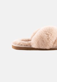 Pantofola morbida beige con parte superiore in pelliccia soffice, design con punta aperta e suola in gomma. Presenta una texture accogliente e una forma arrotondata.