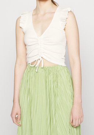 Hvid ribbet crop top med flæseærmer, der har V-hals og centralt skråning, parret med en lysgrøn plisseret nederdel.