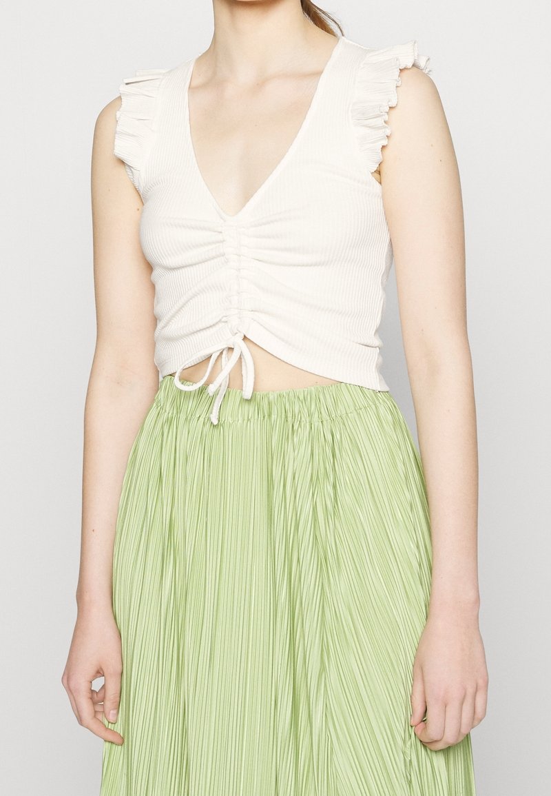 Bílý žebrovaný crop top s volánovými rukávy, s výstřihem do V a centrálním nařasením, zkombinovaný se světle zelenou skládací sukní.