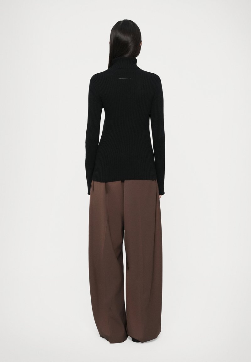 Pull en maille côtelée noir avec col montant et manches longues, présentant une fente au dos. Assorti à un pantalon large marron ample.