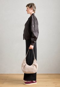 Dark brown bomber jacket, loose black pants, light gray handbag, and burgundy sneakers with white accents. Model facing left.