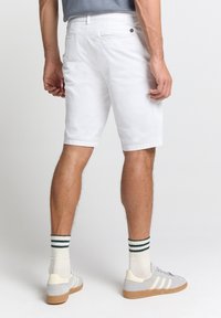 Witte katoenen shorts met een rechte snit, zij- en achterzakken, en een knoopsluiting. Gecombineerd met grijze sneakers en groen gestreepte sokken.