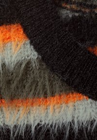 Lähenenud fuzzy kudum kangas mustade, oranžide, hallide ja oliivroheliste geomeetriliste siksakmustritega.