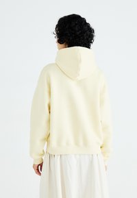 Yellow hoodie with a relaxed fit, featuring a large hood and ribbed cuffs and hem, paired with a flowing light-colored skirt.