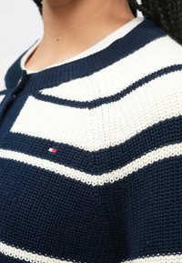 Πλεκτή ζακέτα σε ναυτικό μπλε και λευκές ρίγες, με στρογγυλή λαιμόκοψη, κούμπωμα με κουμπιά και μικρό λογότυπο στο στήθος.