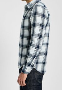 Rutigt skjorta i ljusblå och marinblå, med långa ärmar, knäppning fram och bröstficka. Tillverkad av ett mjukt, strukturerat tyg.