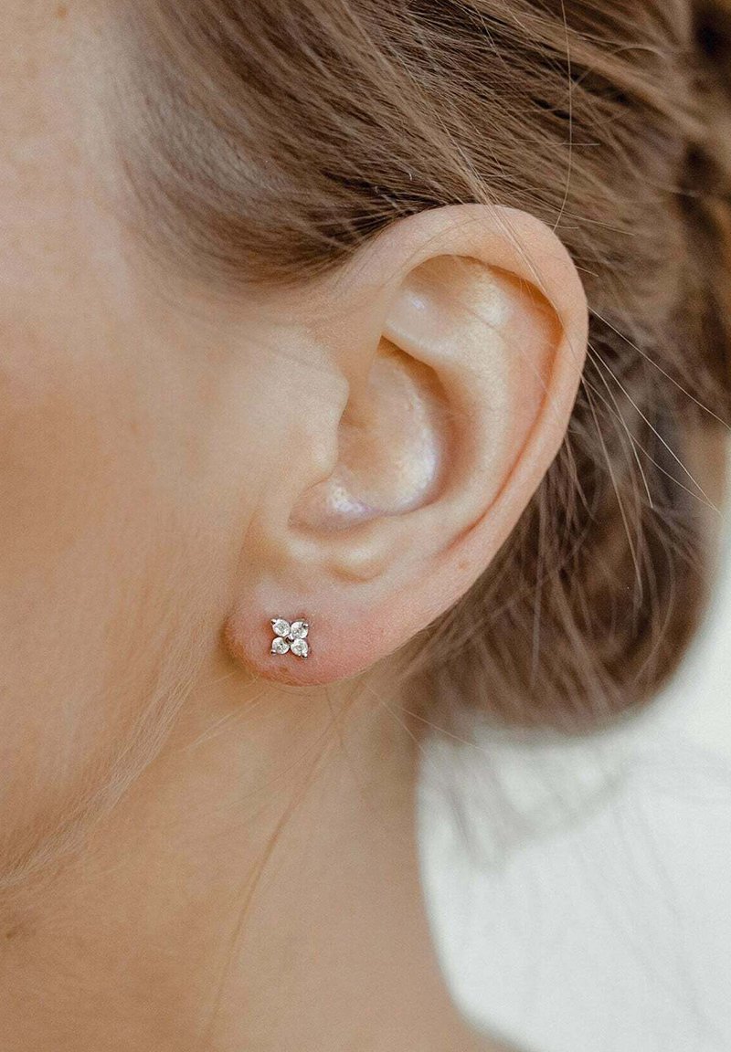 Pendientes de plata con un diseño floral que presentan cuatro piedras preciosas transparentes en una formación de racimo, colocados contra la piel.