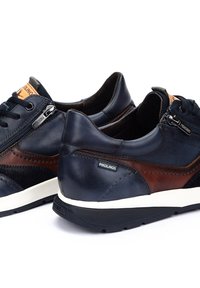 Donkerblauwe en bruine leren sneakers met witte zolen, zijrits, veters en Pikolinos merklabel aan de zijkant en tong.