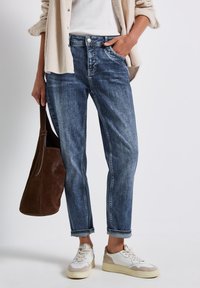 Blauwe denim jeans met een relaxte pasvorm, voorzien van vijf zakken, een knoopsluiting en opgerolde pijpen, gecombineerd met witte sneakers en een bruine tas.