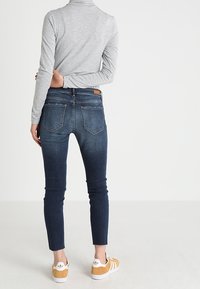 Smala mörkblå denimjeans med ljus blekning och femficksdesign, parat med en grå långärmad tröja och sneakers med gula accenter.