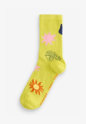 Geltoni raukšlėti kojinės su spalvingais raštais: rožinės žvaigždės, oranžinė saulė ir akies motyvas. Pagamintos iš švelnios, tamprios medžiagos.