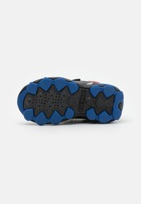 Sole di scarpa sportiva nera con tappi di trazione in gomma blu, dotata di fori di ventilazione e motivi esagonali per aderenza e flessibilità.