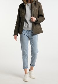 Olivgrön vadderad jacka med huva, grå sweatshirt, ljusblå uppvikta jeans och vita sneakers. Materialet verkar mjukt och varmt.