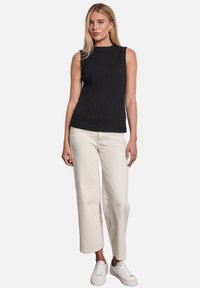 Sort ribbet tanktop, tætsiddende design, parret med cremefarvede brede bukser og hvide sneakers, der står foran en ensfarvet baggrund.